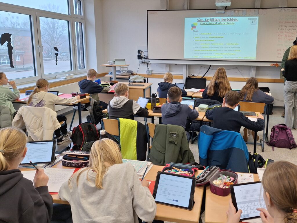 Landrat Marc-André Burgdorf (l.) schaut gemeinsam mit Schulleiterin Thea Wathall Schülerinnen und Schüler über die Schulter beim digitalen Unterricht. Foto: Landkreis Emsland