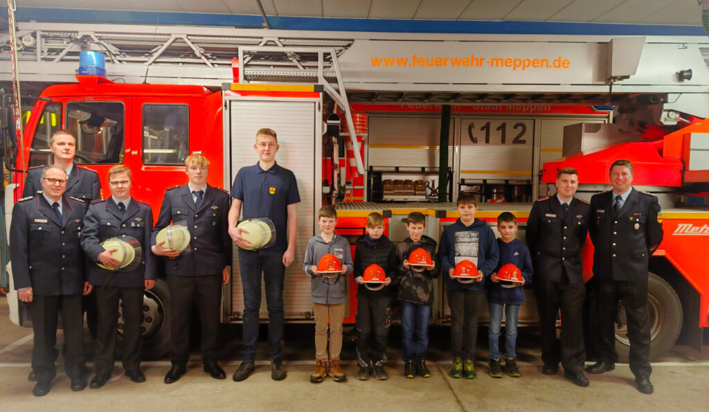 Das Foto zeigt von links nach rechts die Übergaben in die Einsatzabteilung (Feuerwehrhelm) und die Neuaufnahmen in die Jugendfeuerwehr (Jugendfeuerwehrhelm). Foto: Sven Lammers